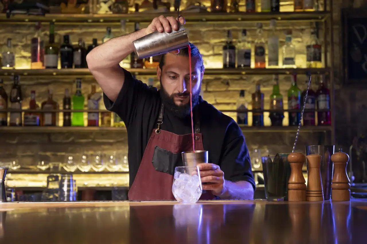 Bartender pours red drink into ice-filled glass