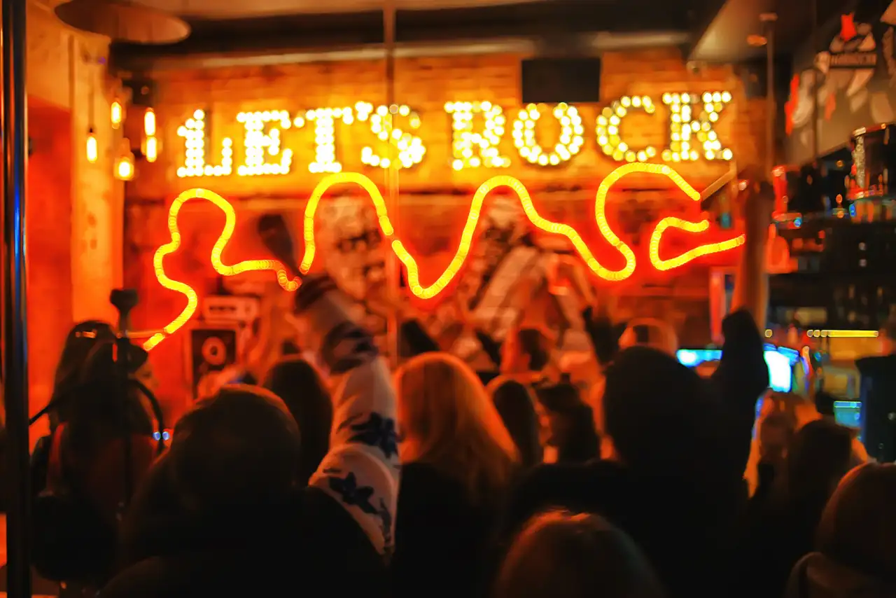 Crowd under neon 'LETS ROCK' sign in a club
