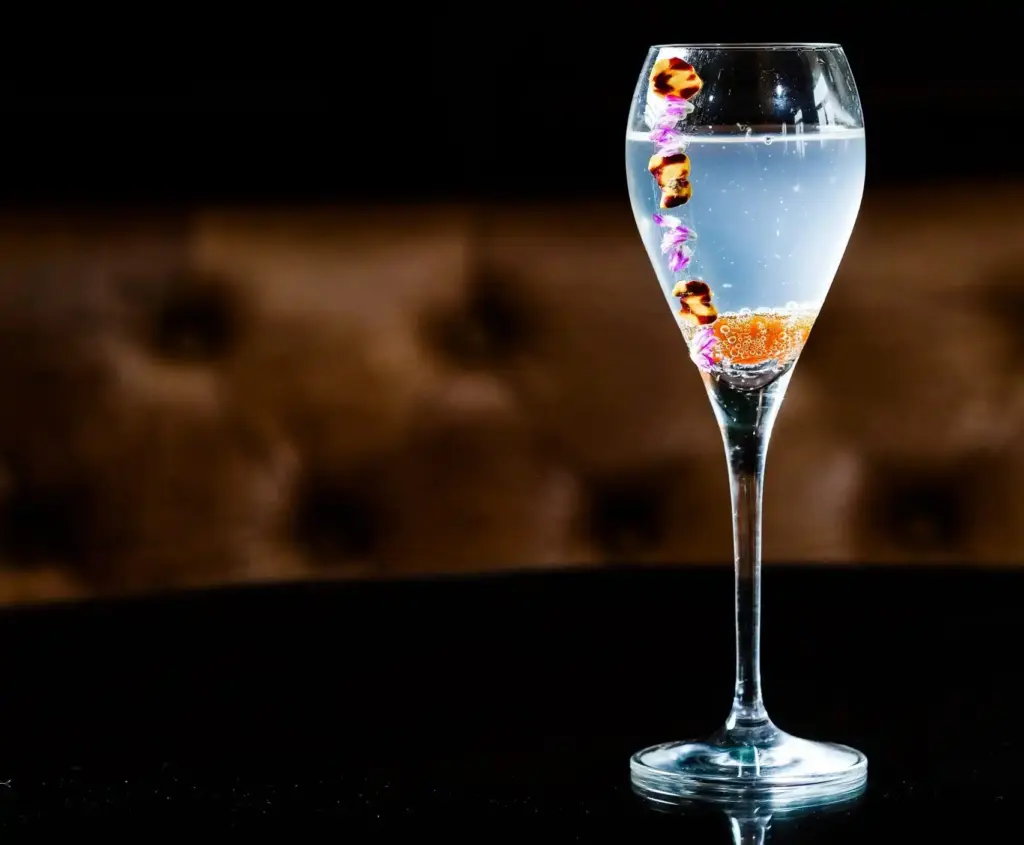 A fancy champagne cocktail garnished with purple edible flowers