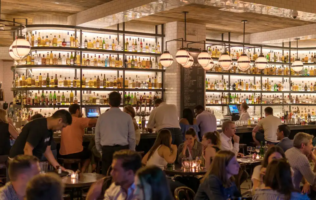Ubud nightlife in stylish bar with warm pendant lights, liquor shelves, and guests enjoying drinks