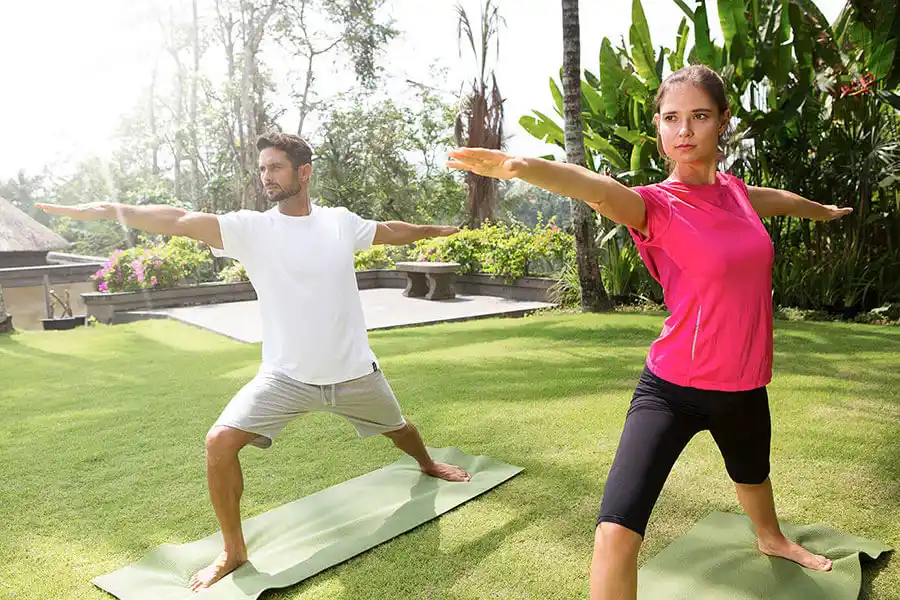 Couple practicing warrior yoga pose on outdoor lawn