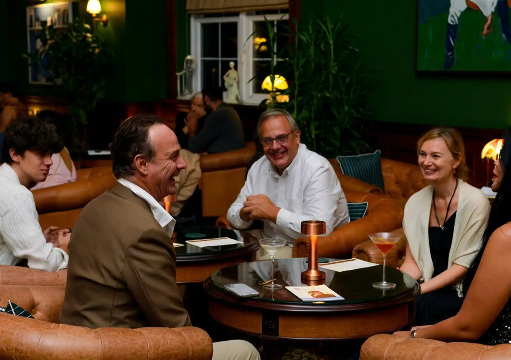 Group enjoying cocktails in stylish lounge with leather chairs and warm lighting