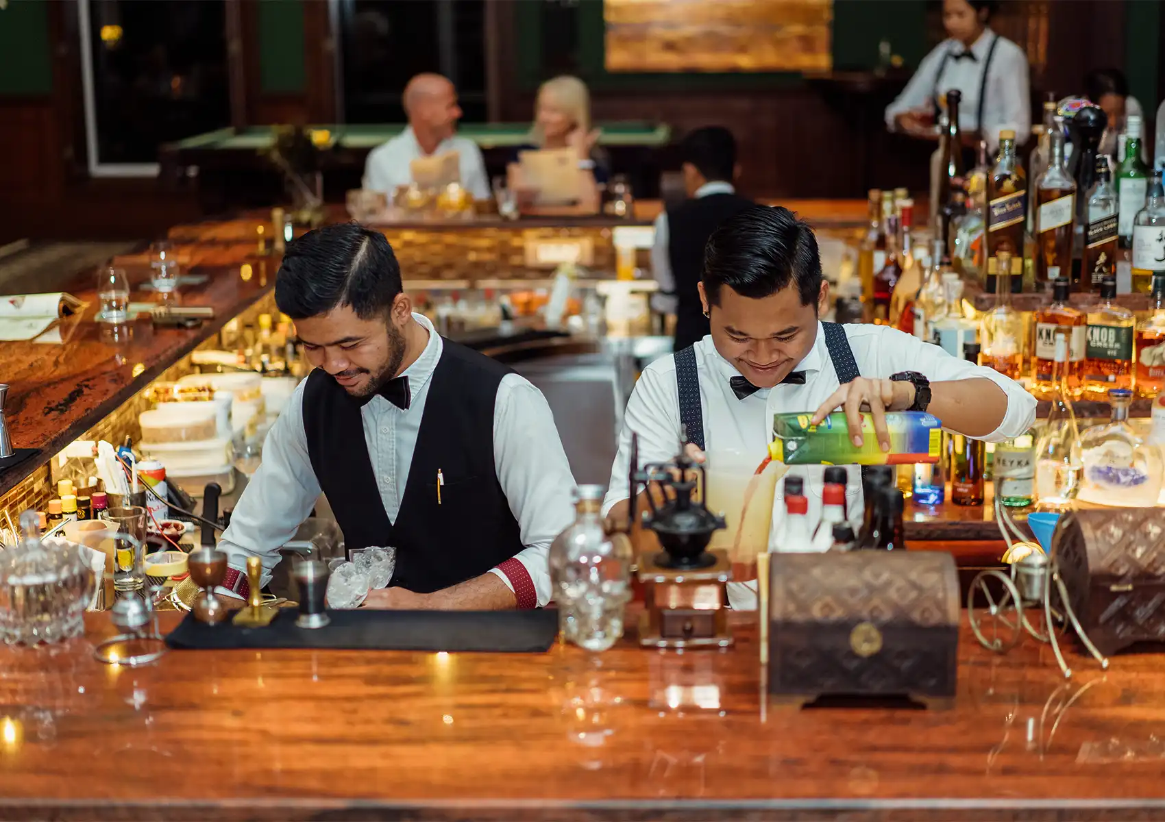 A vast, beautifully illuminated display of premium and diverse liquor bottles resting on the polished wooden counter of a Cocktail Bar Ubud.
