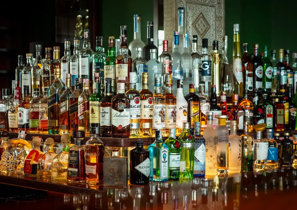 A vast, beautifully illuminated display of premium and diverse liquor bottles resting on the polished wooden counter of a Cocktail Bar Ubud.