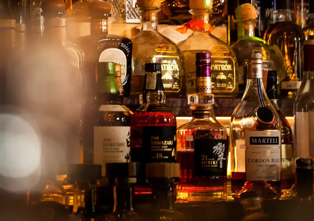 A backlit shelf displaying premium liquor bottles, including Yamazaki and Hibiki whiskies, at a cocktail bar ubud.