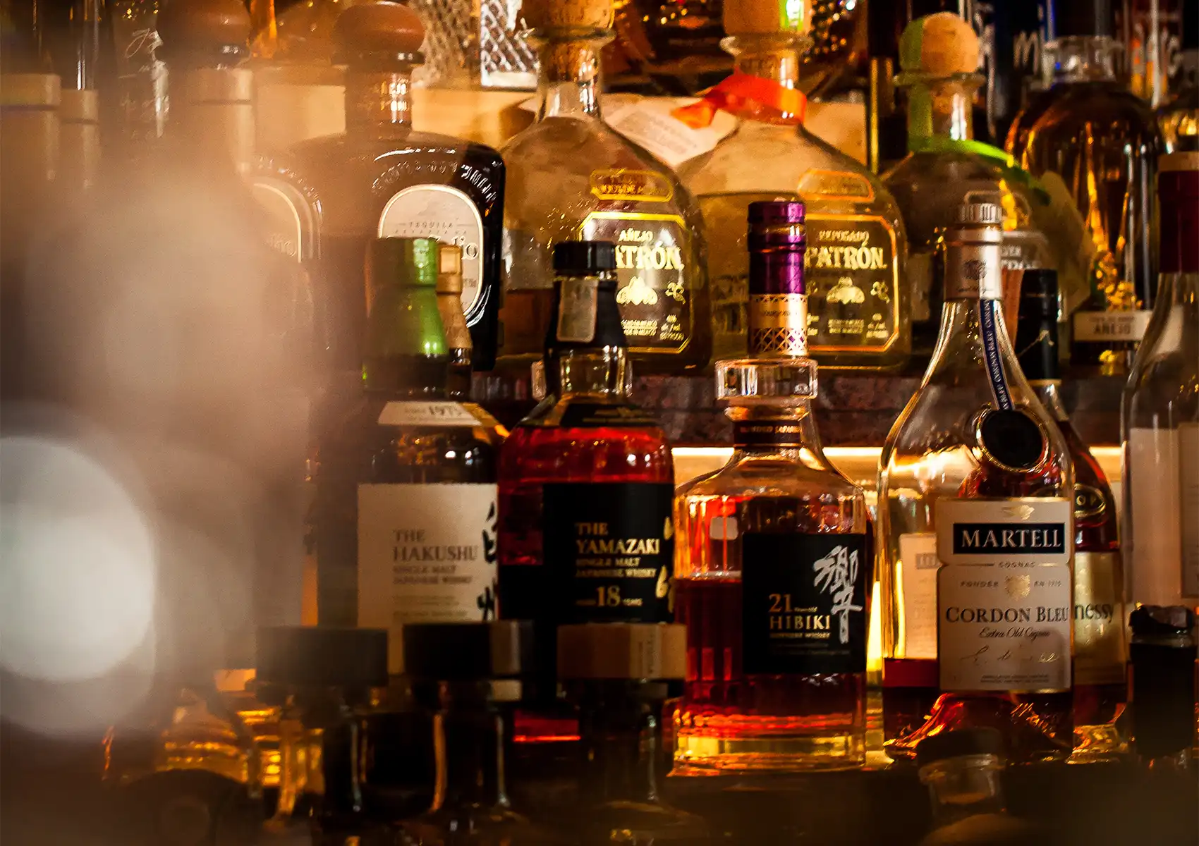A backlit shelf displaying premium liquor bottles, including Yamazaki and Hibiki whiskies, at a cocktail bar ubud.