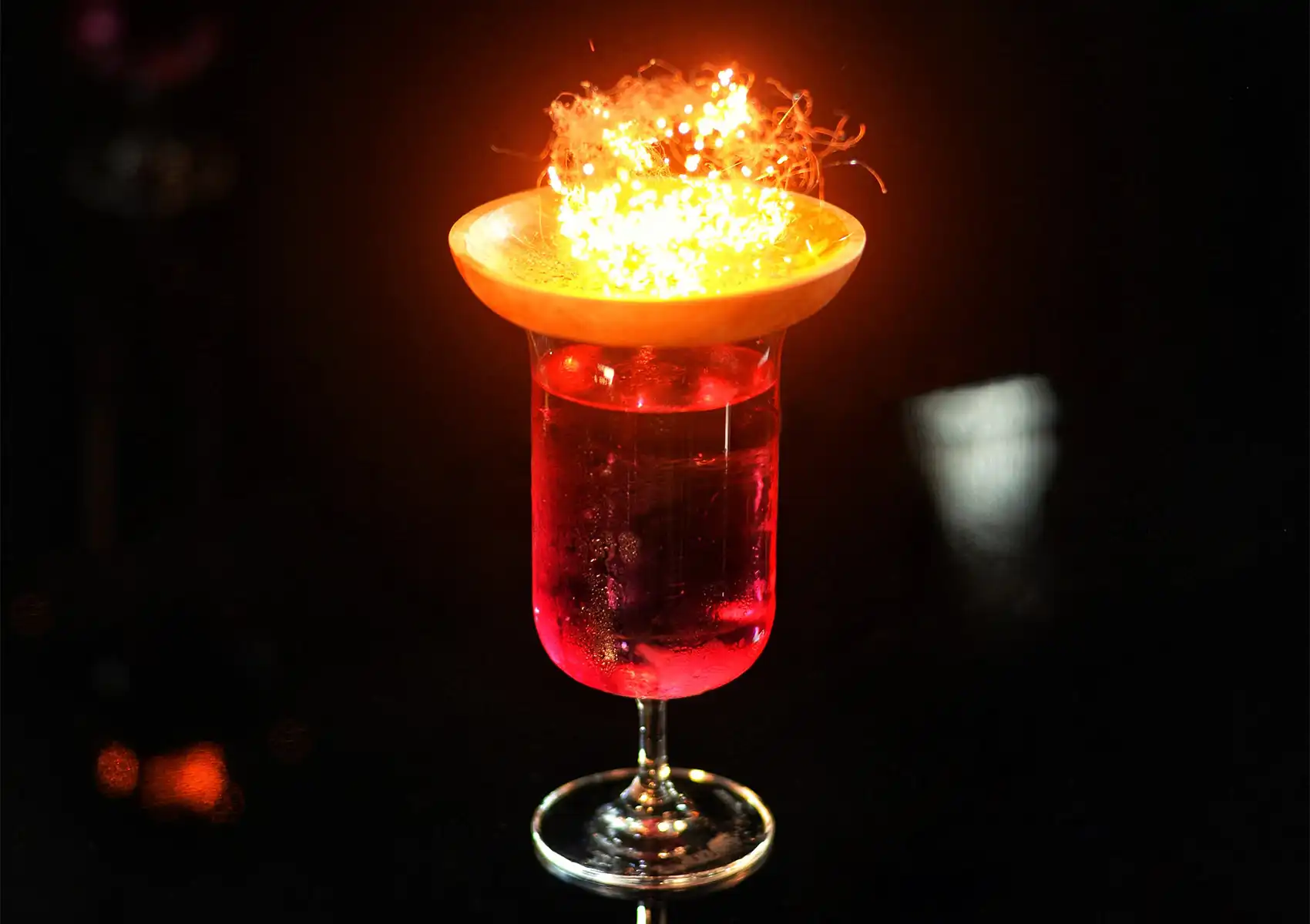 A glowing, theatrical red cocktail served with a flaming garnish at a stylish cocktail bar in Ubud.