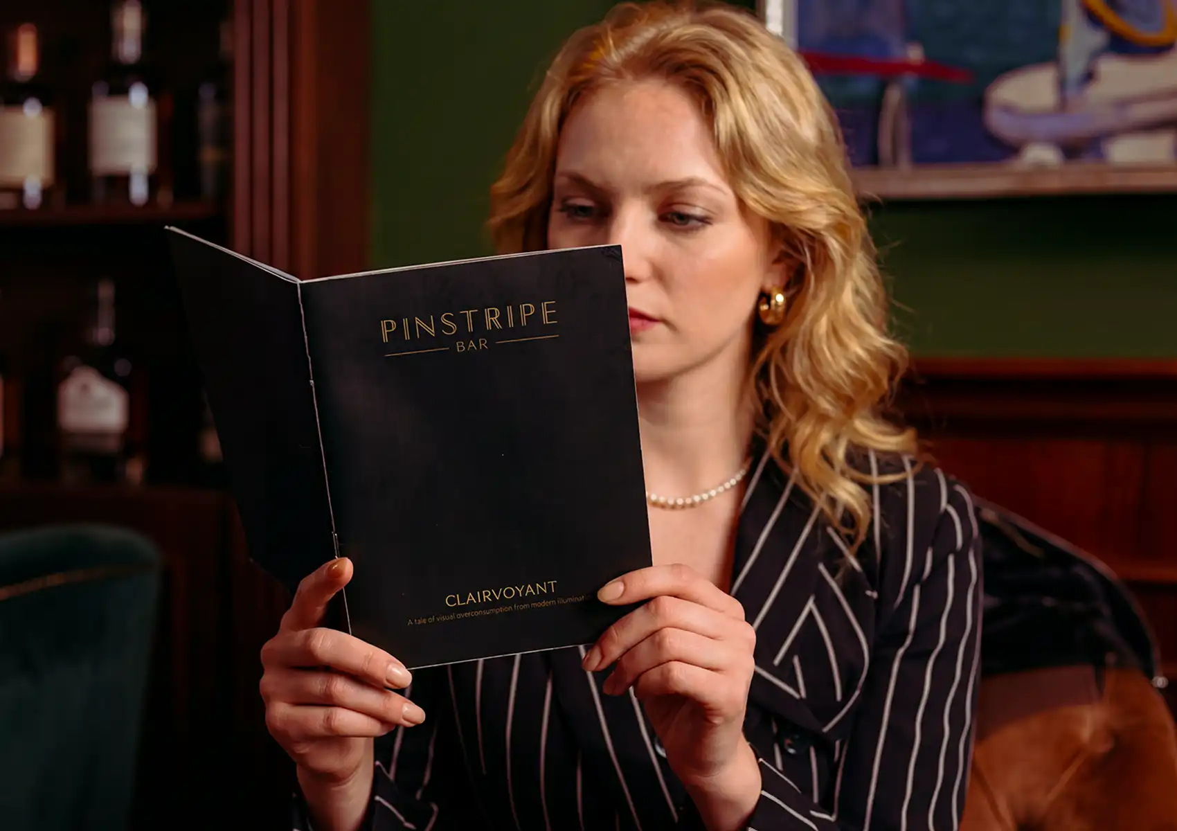 A woman in a striped blazer reading a Pinstripe Bar menu at a cocktail bar Ubud.