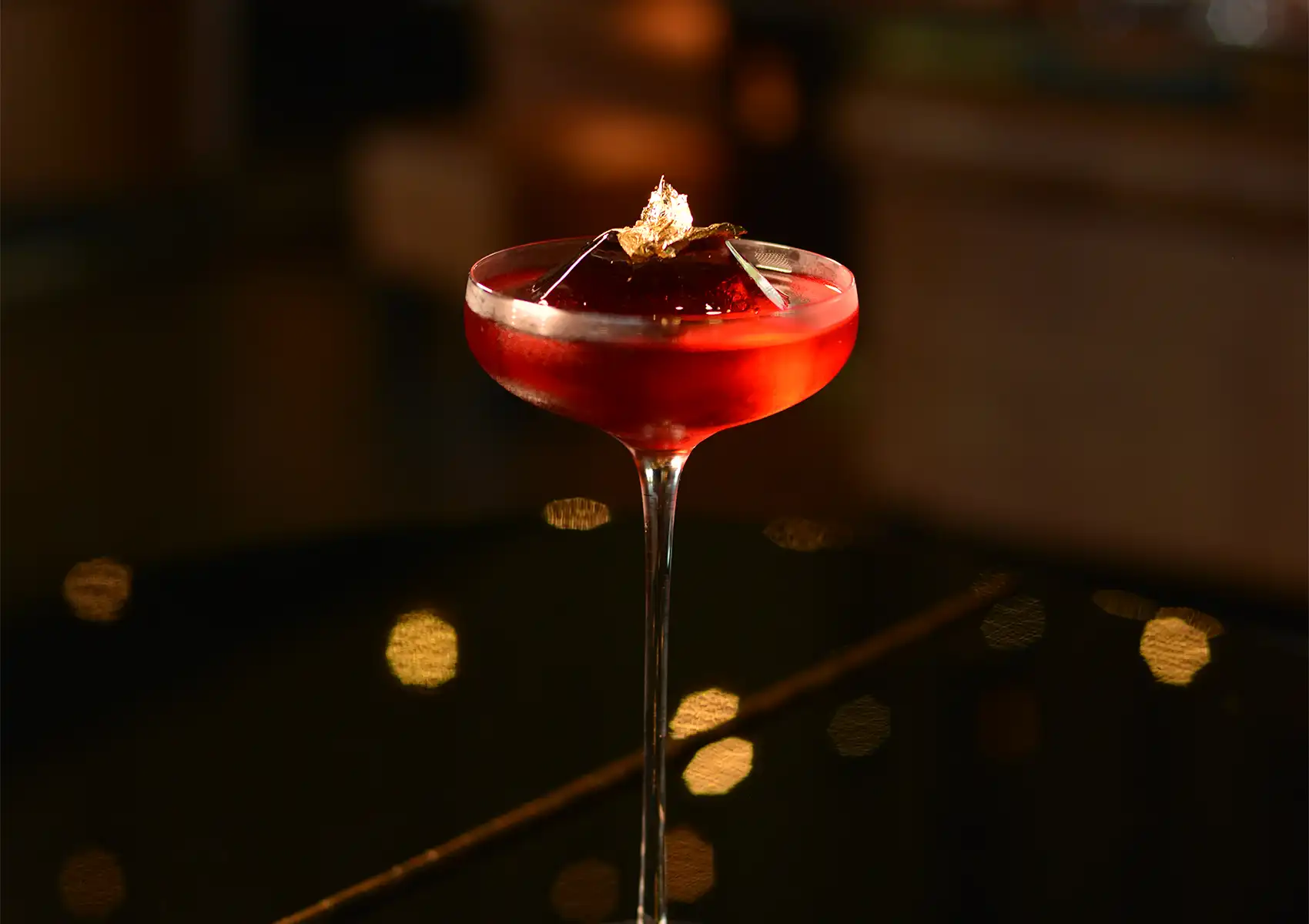 A close-up of a vibrant red signature cocktail featuring a large ice cube topped with gold leaf in an elegant glass at a cocktail bar ubud.