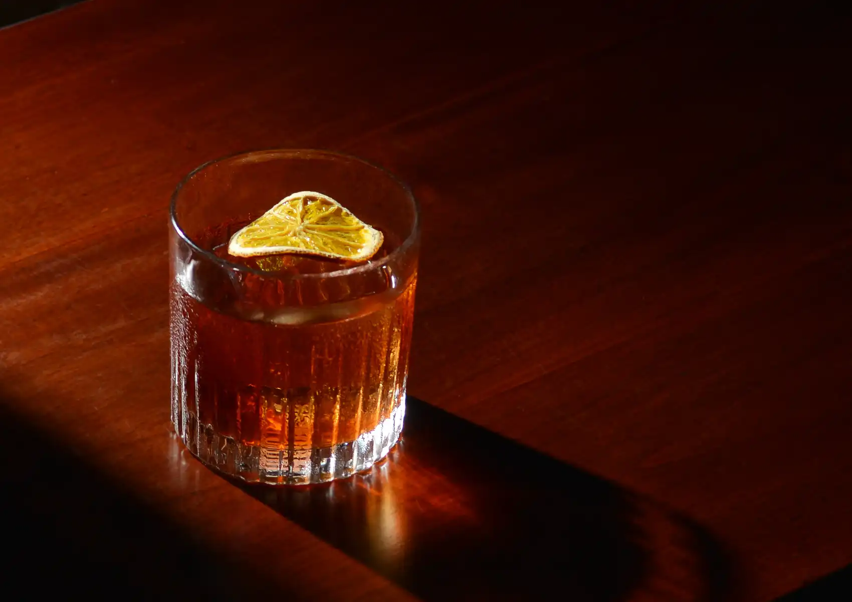 A classic Negroni cocktail over ice, garnished with a dried citrus wheel, resting on a polished dark wooden counter at a cocktail bar ubud.