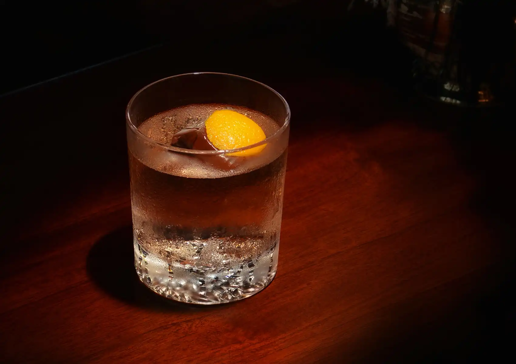 A clarified, crystal-clear Negroni served over a single large ice cube and garnished with an orange twist on a dark wooden counter at a premium cocktail bar Ubud.