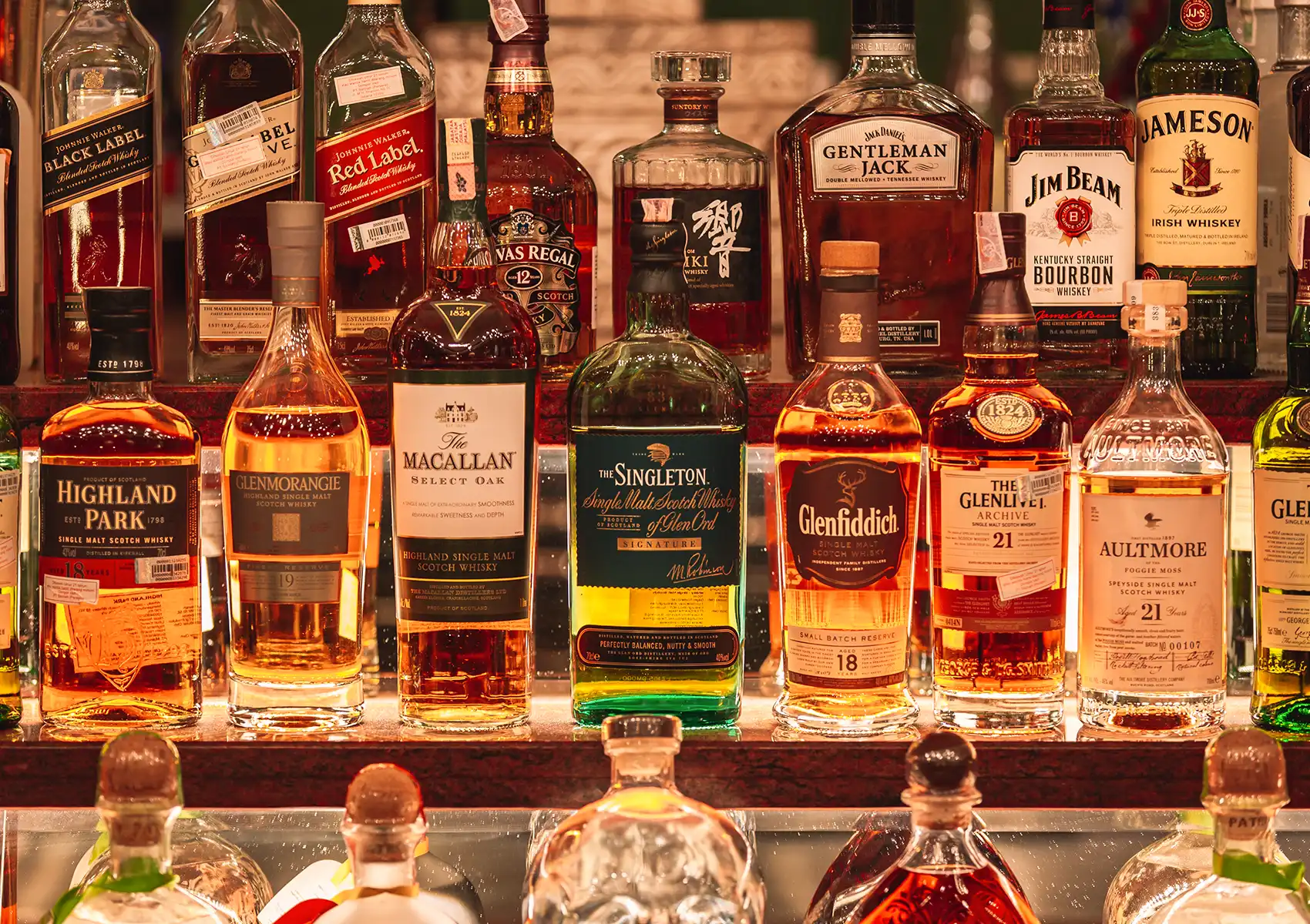 An extensive, brightly lit display of premium whisky and liquor bottles arranged on glass shelves at a cocktail bar ubud.