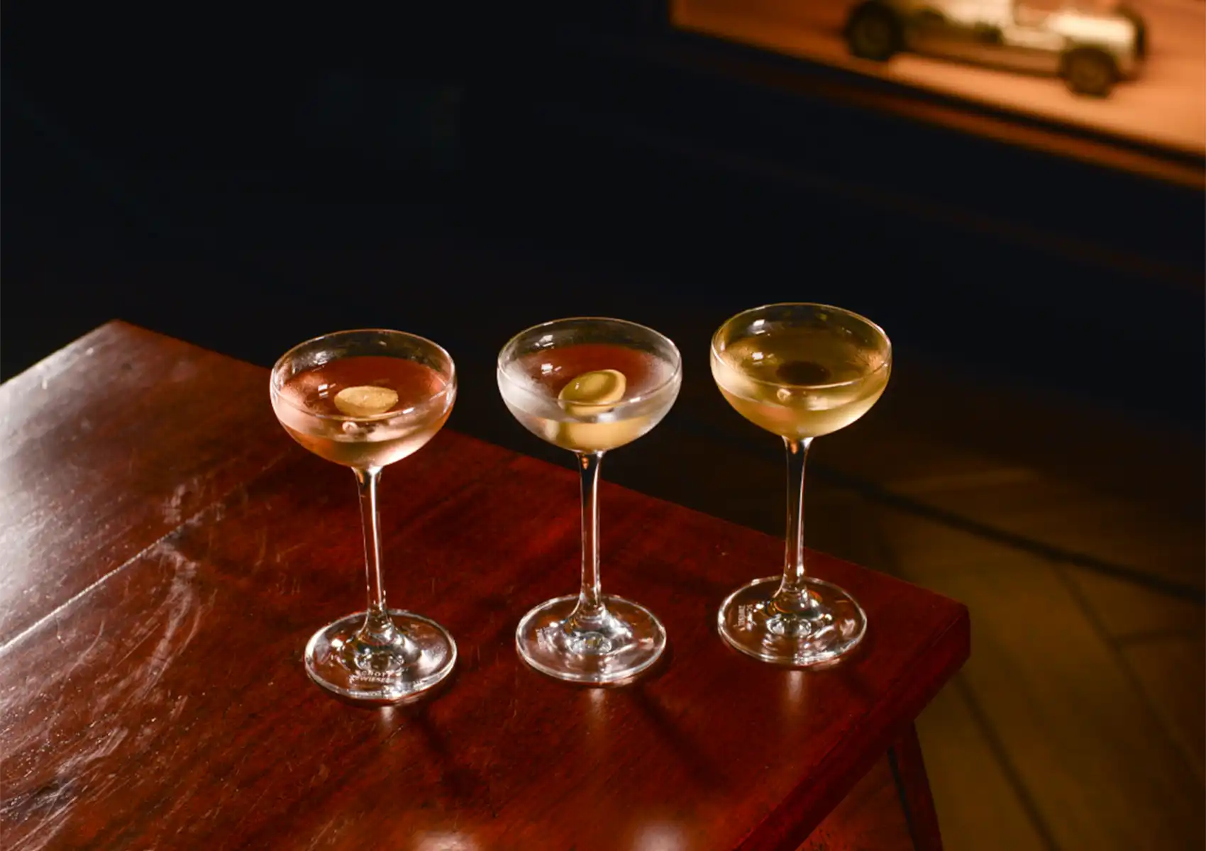 Three crafted drinks in elegant coupe glasses resting on a dark wooden table at a sophisticated cocktail bar ubud.