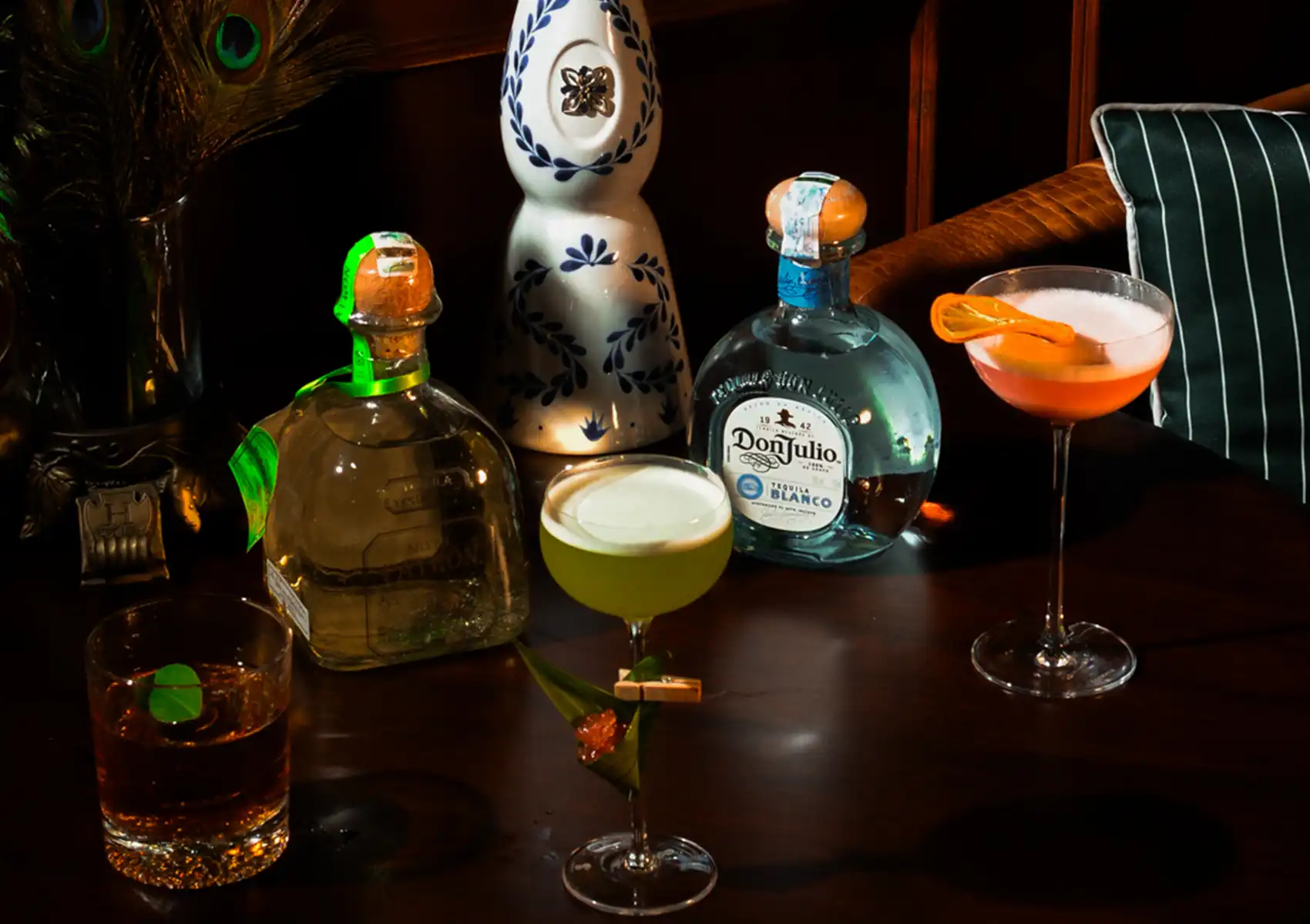 A selection of three crafted tequila drinks alongside premium tequila bottles displayed on a dark wooden table at a cocktail bar ubud.